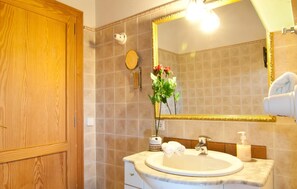 Un bagno con una porta in legno, un lavabo in marmo, uno specchio con cornice dorata, un porta asciugamani e un vaso con fiori.