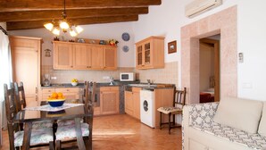 A cozy kitchen with wooden cabinets, a dining table with chairs, a washing machine, and a sofa in a living area. - Lovely home in Colonia de Sant Jordi (Colonia de Sant Jordi)