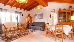 Una sala de estar acogedora con sofá, mesa de comedor y sillas, vigas de techo de madera y un aparador con puertas de cristal.