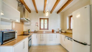 A modern kitchen with white cabinets, a built-in oven, a microwave, and a refrigerator. There is a window with wooden frames and a hanging light fixture. - Luxurious home in Manacor with private swimming pool, can be inside or outside (Manacor)