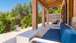 Een terras buiten met een houten pergola, een blauwe bank en een witte tafel met glazen.