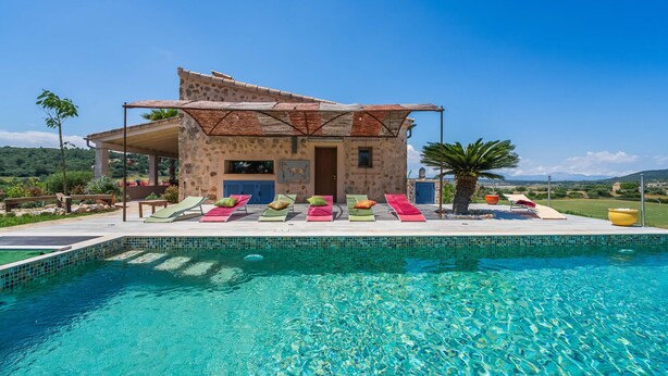 Un edificio de piedra con piscina, mobiliario de exterior y vistas al campo.