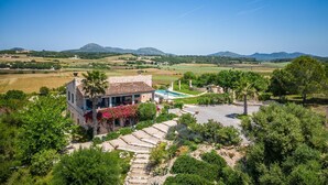 Una villa de piedra con piscina, rodeada de exuberante vegetación y campos.