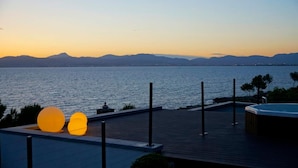 Una terraza frente al agua con jacuzzi, un pasillo de madera y dos esculturas esféricas iluminadas.