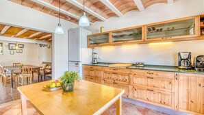 A modern kitchen with wooden cabinets, a dining area with a wooden table, and a ceiling with exposed beams. - Amazing home in Sant Llorenc (Sant Llorenc)