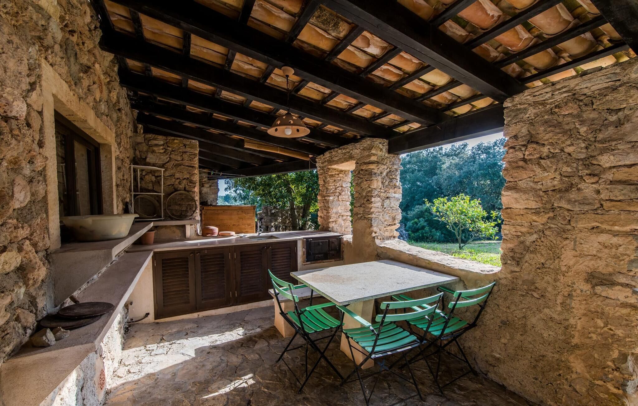 Un espace cuisine extérieur doté de murs en pierre, d’un plafond en bois et d’une table avec des chaises.