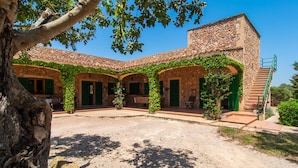 Un edificio de piedra con contraventanas verdes y un patio cubierto.