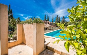 Une piscine entourée de verdure et d’un mur de pierre, avec un ciel bleu dégagé au-dessus.