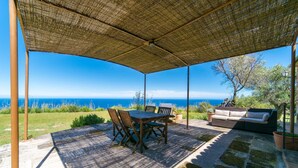 Een overdekt terras met een tafel, stoelen en een bank, en uitzicht op zee.