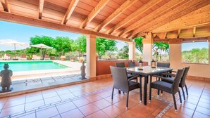 Eine überdachte Terrasse mit Pool, Sitzgelegenheiten im Freien und Blick auf Grünflächen.
