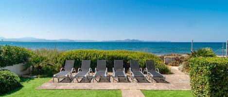 Un patio con seis sillones de descanso frente al mar.