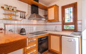 Eine Küche mit Herd, Backofen, Geschirrspüler und einem Fenster mit Blick auf Grünflächen.