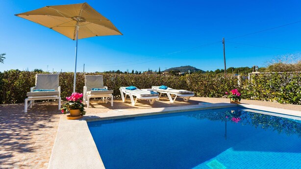 Ein Pool mit Liegestühlen und Sonnenschirm, umgeben von Grünflächen und blauem Himmel.