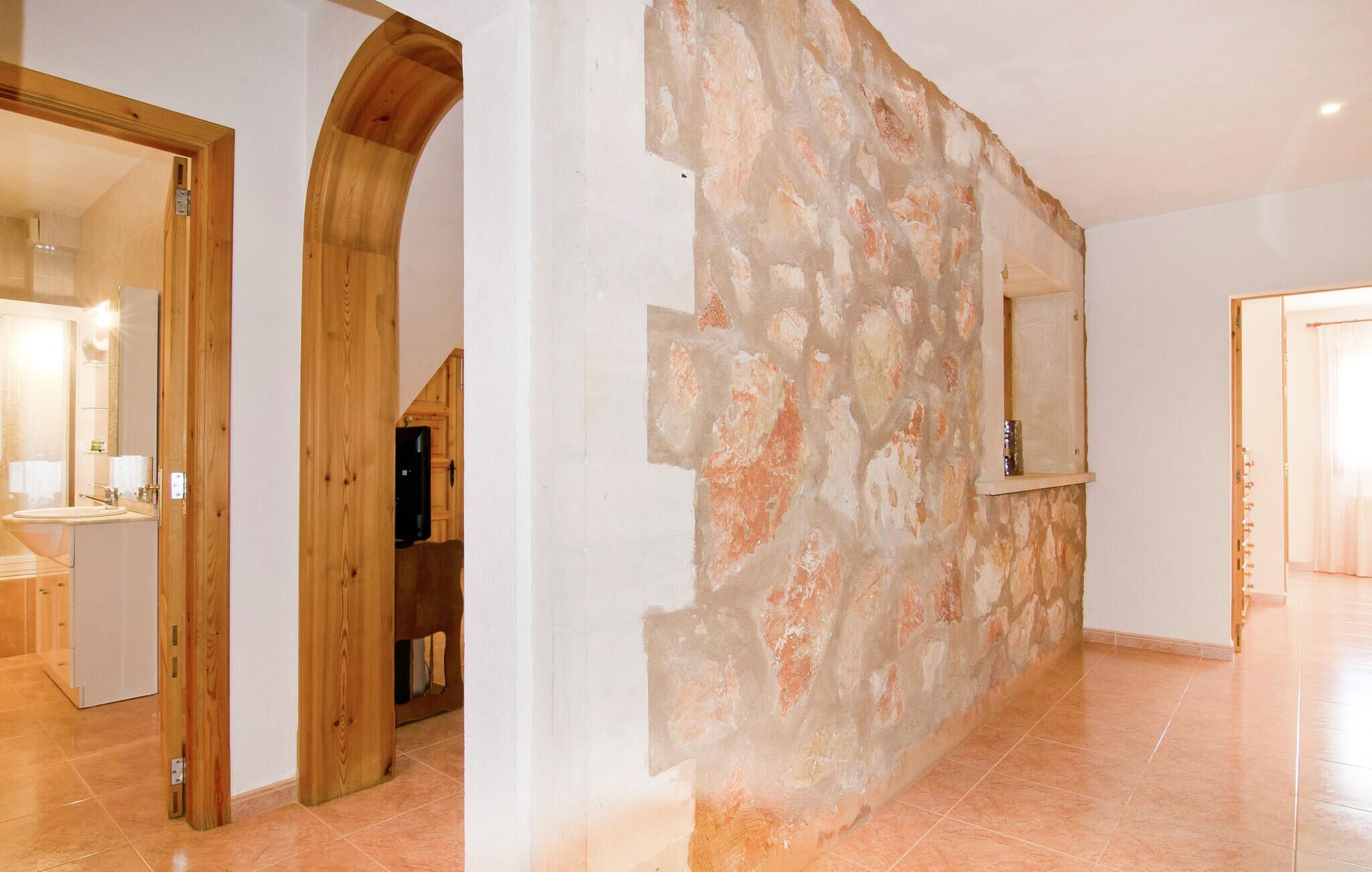 Un couloir avec un mur en pierre, des encadrements de porte en bois et un sol carrelé.