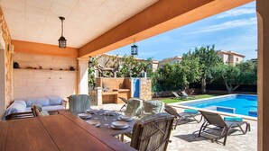 Ein Essbereich im Freien mit Pool, Korbstühlen und einem Holztisch, gedeckt für eine Mahlzeit.