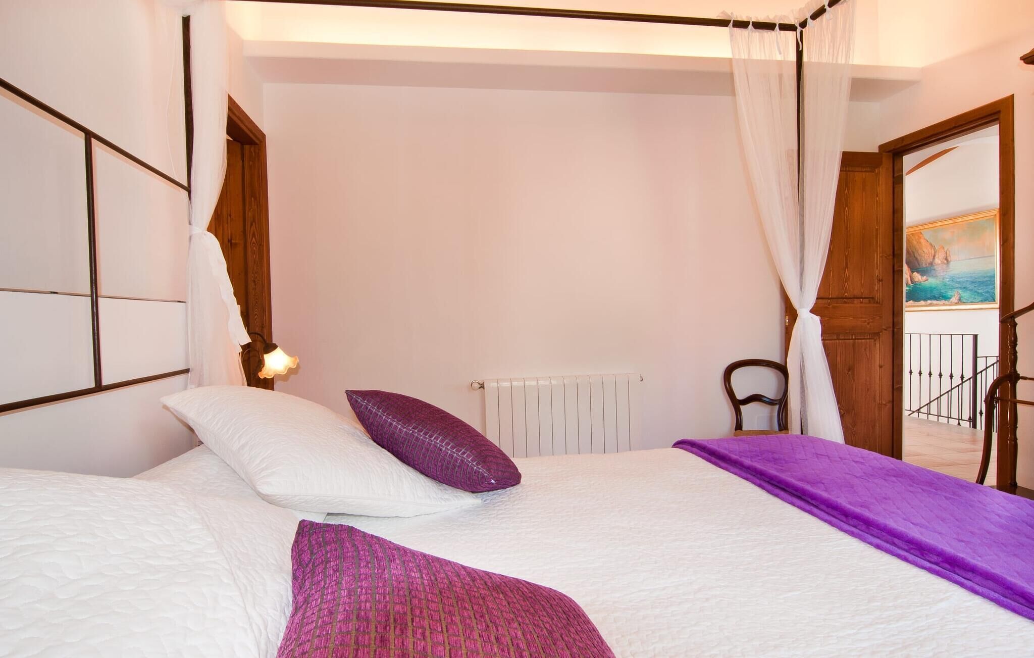 A bedroom with a bed, a radiator, a chair, and a painting on the wall.
