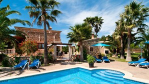Un área de piscina con sillones de descanso, un edificio de piedra y palmeras.