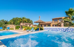 Zona de piscina con sillones de descanso, una bañera de hidromasaje y un edificio de piedra con piscina azulejada.