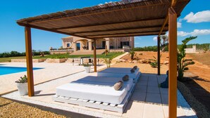 Un espacio de descanso cubierto al aire libre con piscina, un edificio de piedra al fondo y un jardín ajardinado.