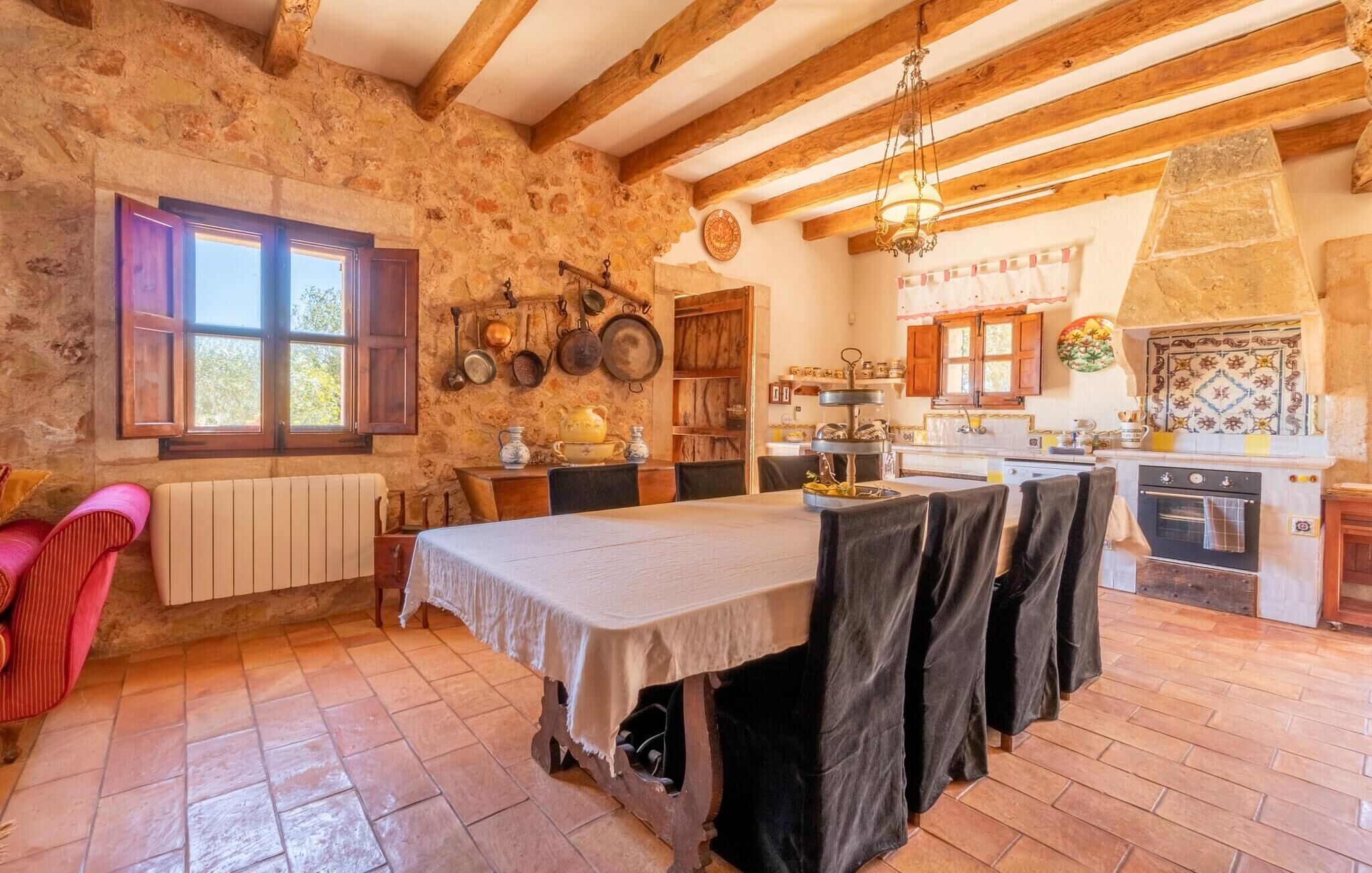 Una cocina rústica con paredes de piedra vista, vigas de madera y una amplia mesa de comedor con sillas.