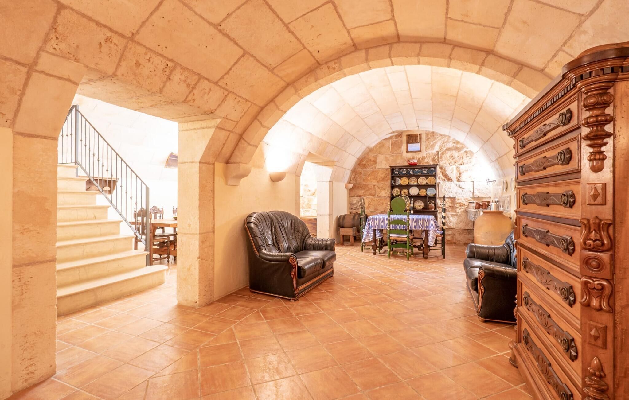 A spacious room with a stone arch ceiling, a fireplace, a wooden cabinet with drawers, and a dining area with a staircase.
