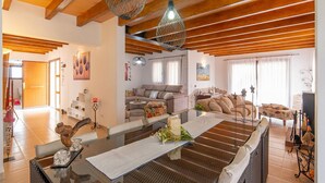 Een ruime woonkamer met een houten plafond, een zithoek, een eettafel met een vaas, en een keuken in de achtergrond.