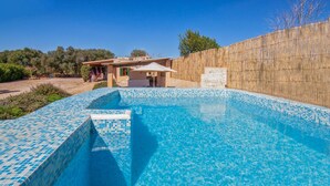 A swimming pool with blue mosaic tiles, a wooden fence, and a building with a patio in the background. - Stunning home in Ses Salines (Ses Salines)