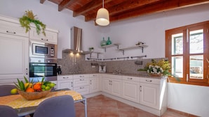 A kitchen with white cabinets, a granite countertop, a microwave, an oven, and a sink. There is a window with a view of the outside. - Stunning home in Ses Salines (Ses Salines)