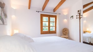 Um quarto com uma cama grande, teto de madeira, janela com cortinas, uma cadeira e um espelho.