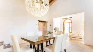 A dining area with a glass table, white chairs, and a chandelier. There is a stone wall and a doorway leading to another room. - Nice home in Sant Llorenc with private swimming pool, can be inside or outside (Sant Llorenc)