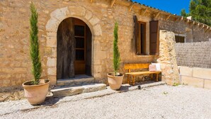 A stone building with an arched doorway, a bench, and two potted plants. - Nice home in Sant Llorenc with private swimming pool, can be inside or outside (Sant Llorenc)