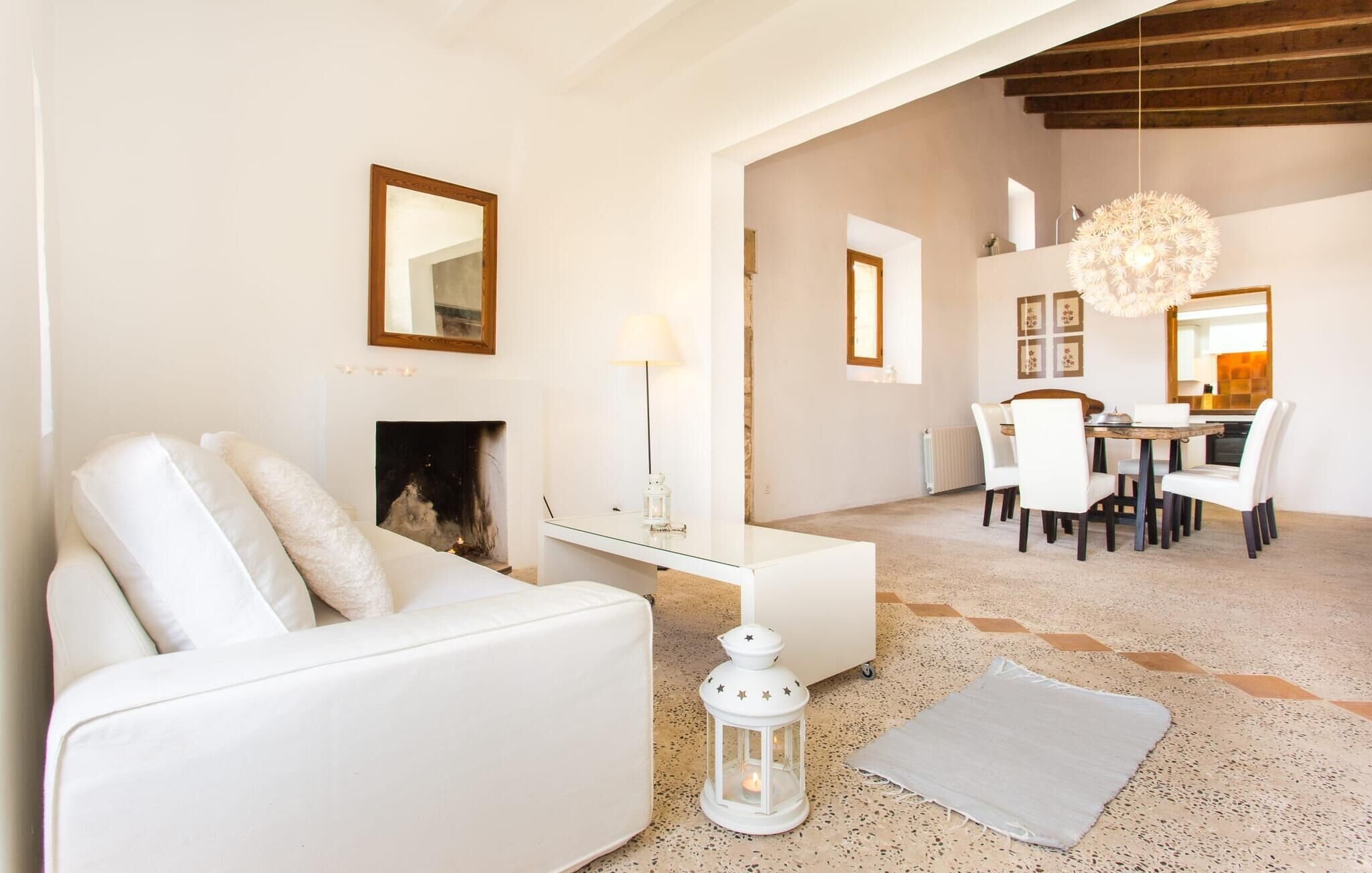 Un salon moderne avec un canapé blanc, une cheminée, un coin repas avec une table et des chaises, et une cuisine en arrière-plan.