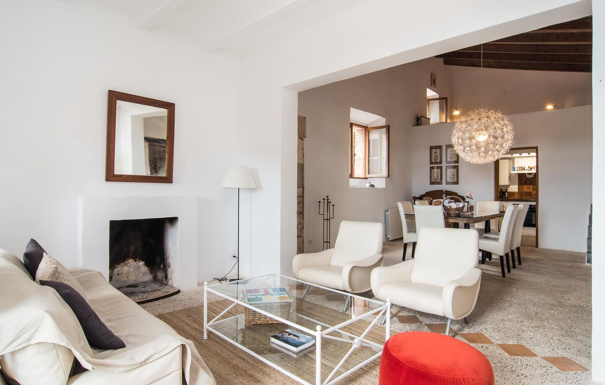 A modern living room with a glass coffee table, white sofas, a fireplace, and a dining area with a chandelier.