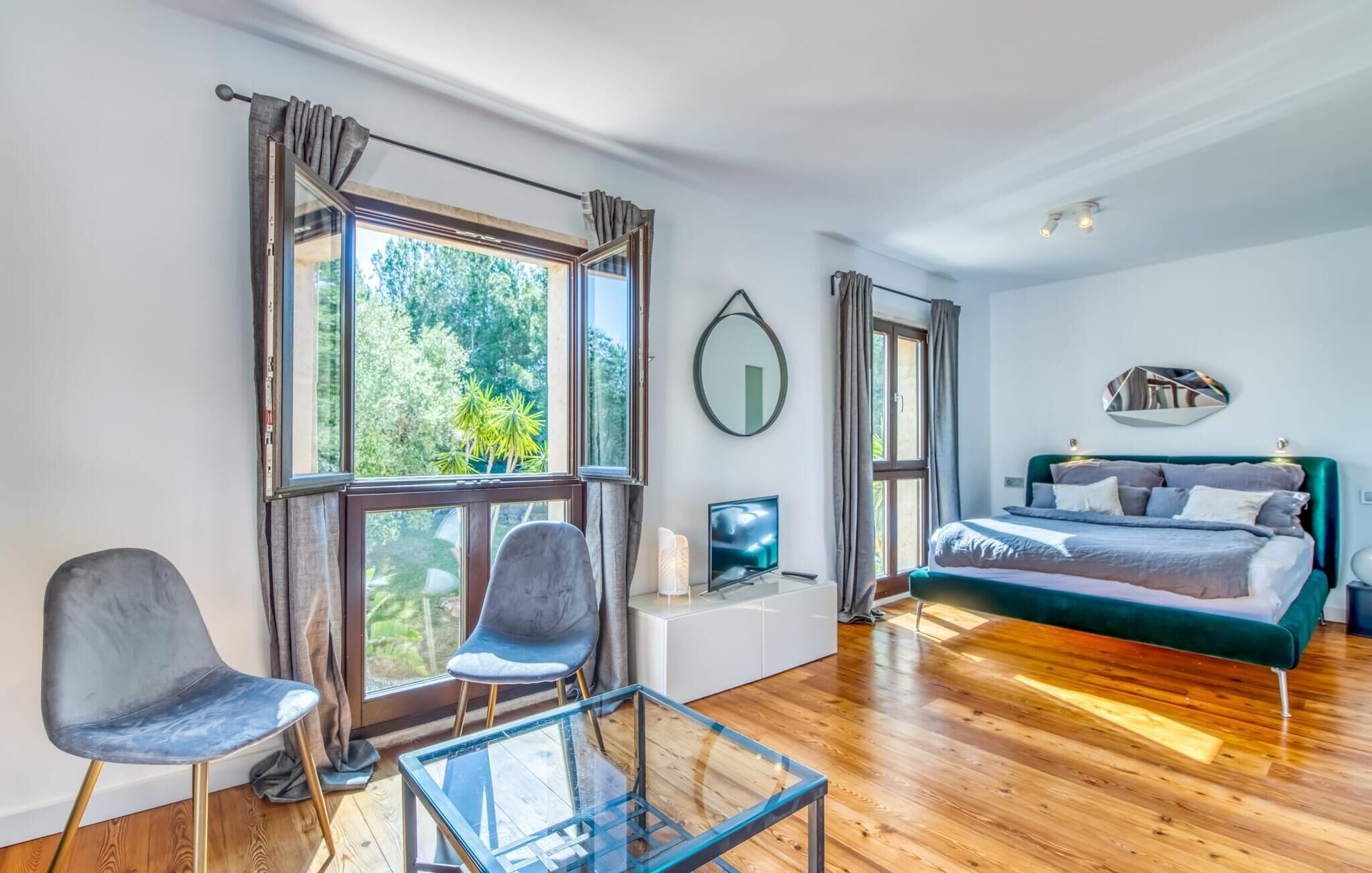 Une chambre moderne avec un grand lit, deux fauteuils, une table en verre et un téléviseur.