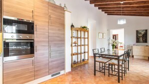 A modern kitchen with wooden cabinets, built-in ovens, and a dining area with a glass table and chairs. - Cozy home in Arta with private swimming pool, can be inside or outside (Arta)