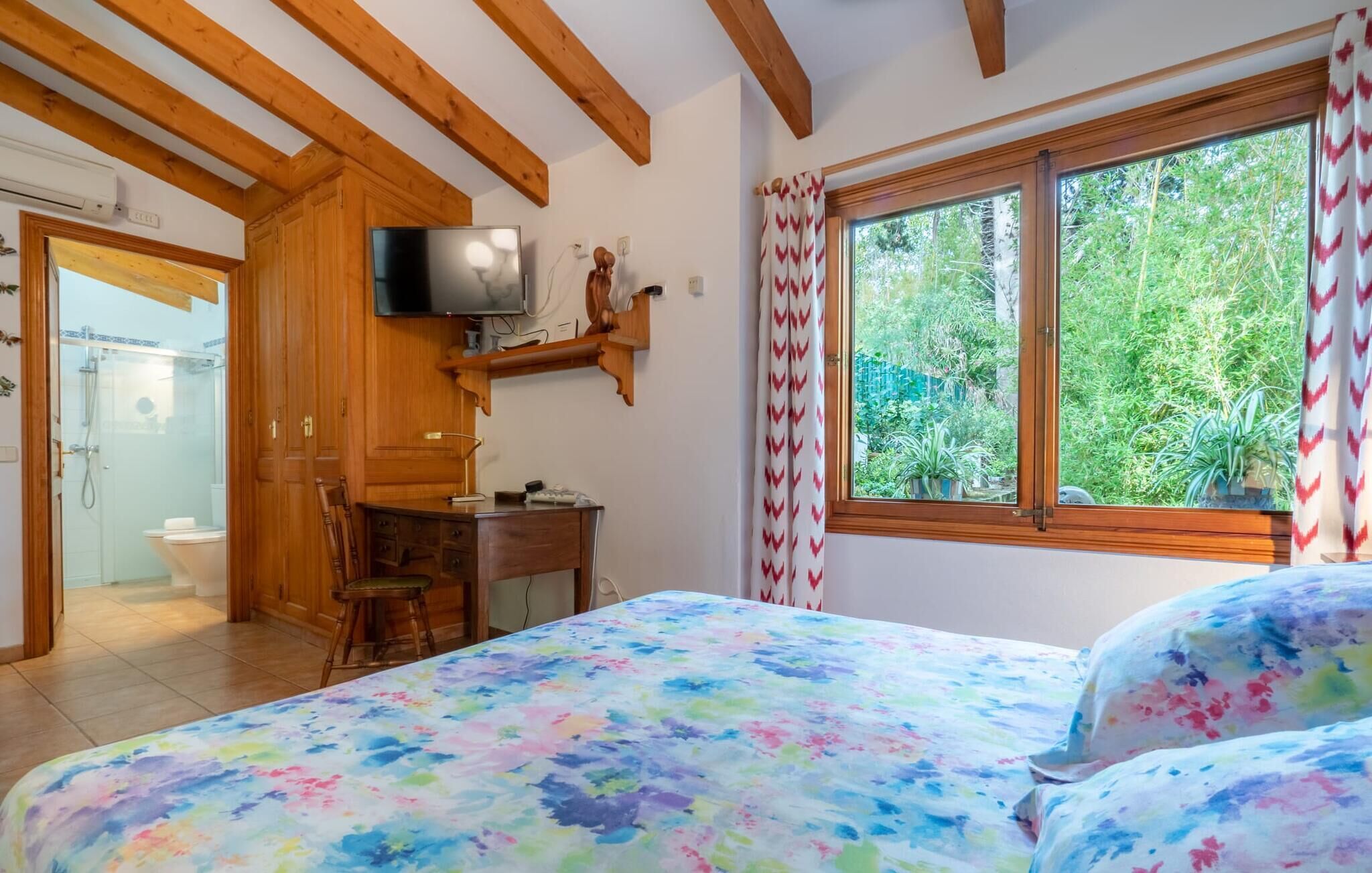 Un dormitorio con una cama, un escritorio, un televisor y una ventana con cortinas.