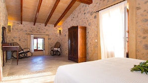 Un dormitorio con una cama, un armario de madera, dos sillas, una mesa y una pared de piedra.
