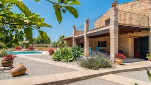 Un edificio de piedra con piscina, mobiliario de exterior y plantas en macetas.