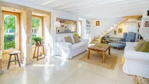 Uma sala de estar espaçosa com um sofá branco, uma mesa de centro de madeira e uma escada que leva a um andar superior.