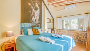 A bedroom with a large bed, a nightstand, a lamp, a painting, a stone wall, and a window with curtains. - Awesome home in Inca with private swimming pool, can be inside or outside (Inca)