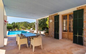 Une terrasse extérieure avec une piscine, une table et des chaises, et une vue sur la végétation environnante.