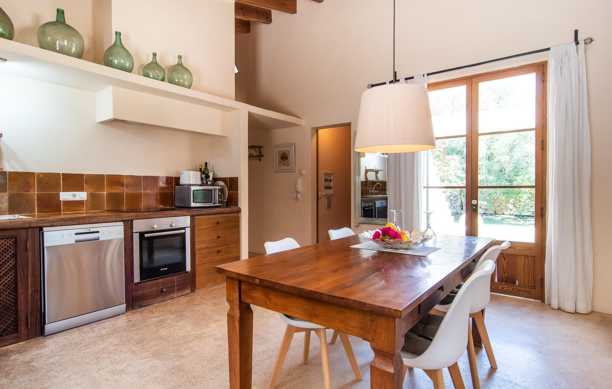 Una cocina moderna con una mesa y sillas de madera, una lámpara colgante y vistas al exterior a través de un amplio ventanal.