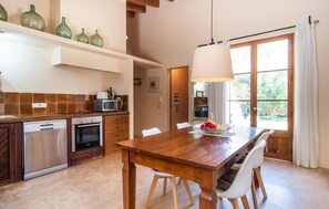 Une cuisine moderne avec une table et des chaises en bois, un luminaire suspendu et une vue sur l’extérieur grâce à une grande fenêtre.