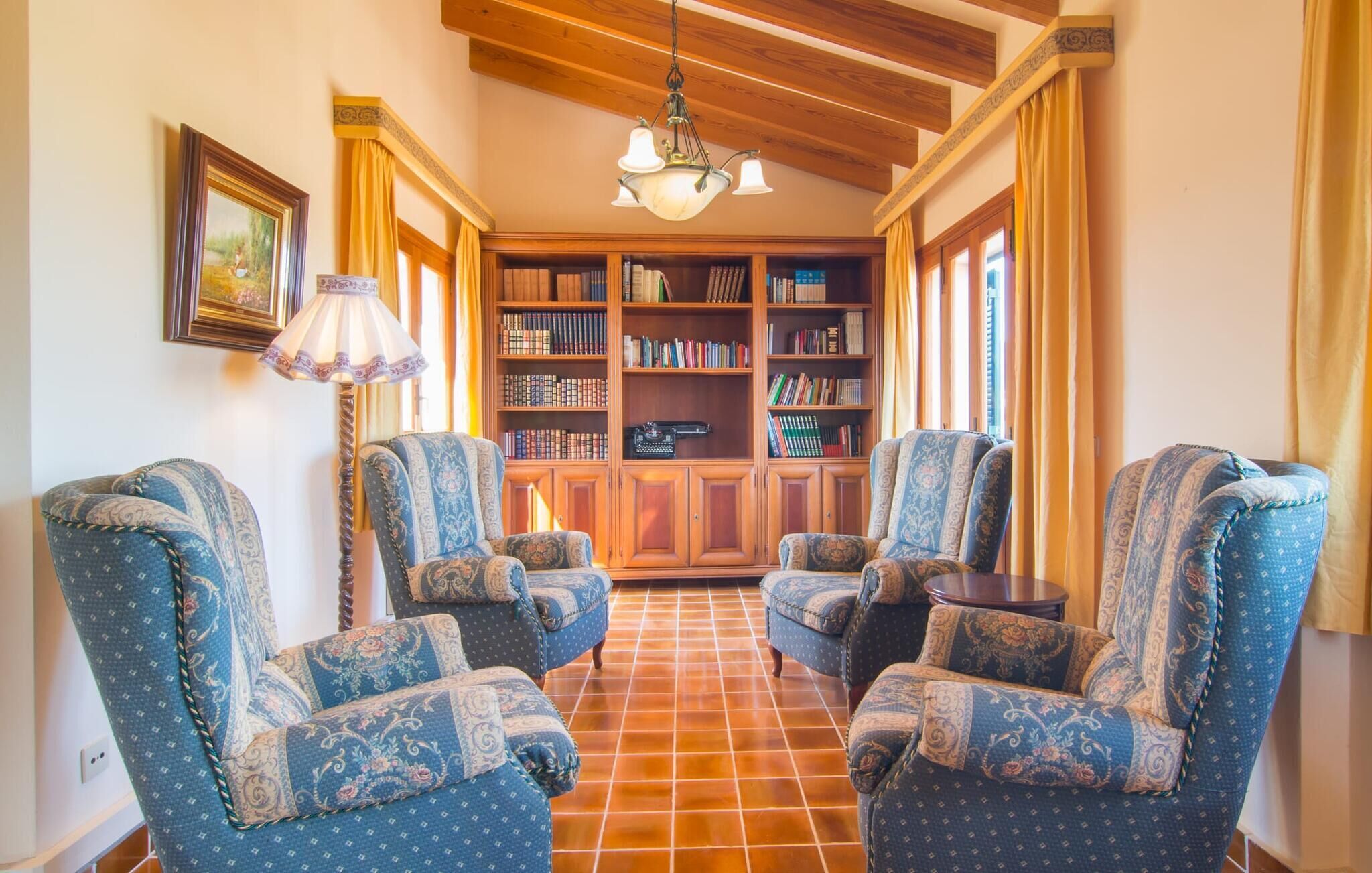A library with four patterned armchairs, a wooden bookshelf, and a hanging lamp.