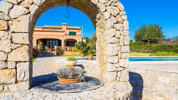 A stone archway leading to a pool area with a house in the background. - Beach front home in Port Verd (Port Verd)