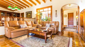 A spacious living room with a large leather sectional sofa, a wooden coffee table, and a patterned rug. There is a staircase with wooden railings leading to an upper floor. - Beach front home in Port Verd (Port Verd)
