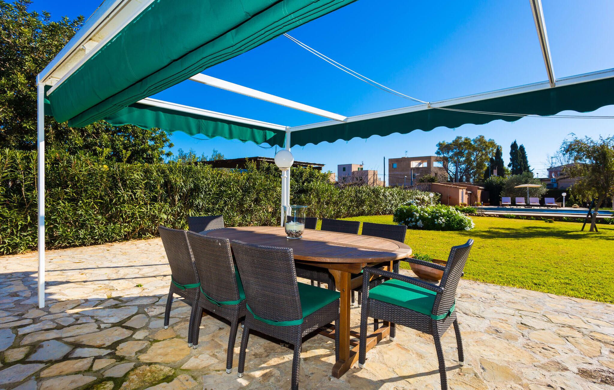 An outdoor patio with a round table and wicker chairs, a green umbrella, and a stone floor.