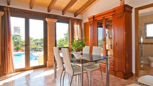 A dining area with a glass table and chairs, a wooden cabinet, and a view of a swimming pool. - Beautiful home in Ariany with private swimming pool, can be inside or outside (Ariany)
