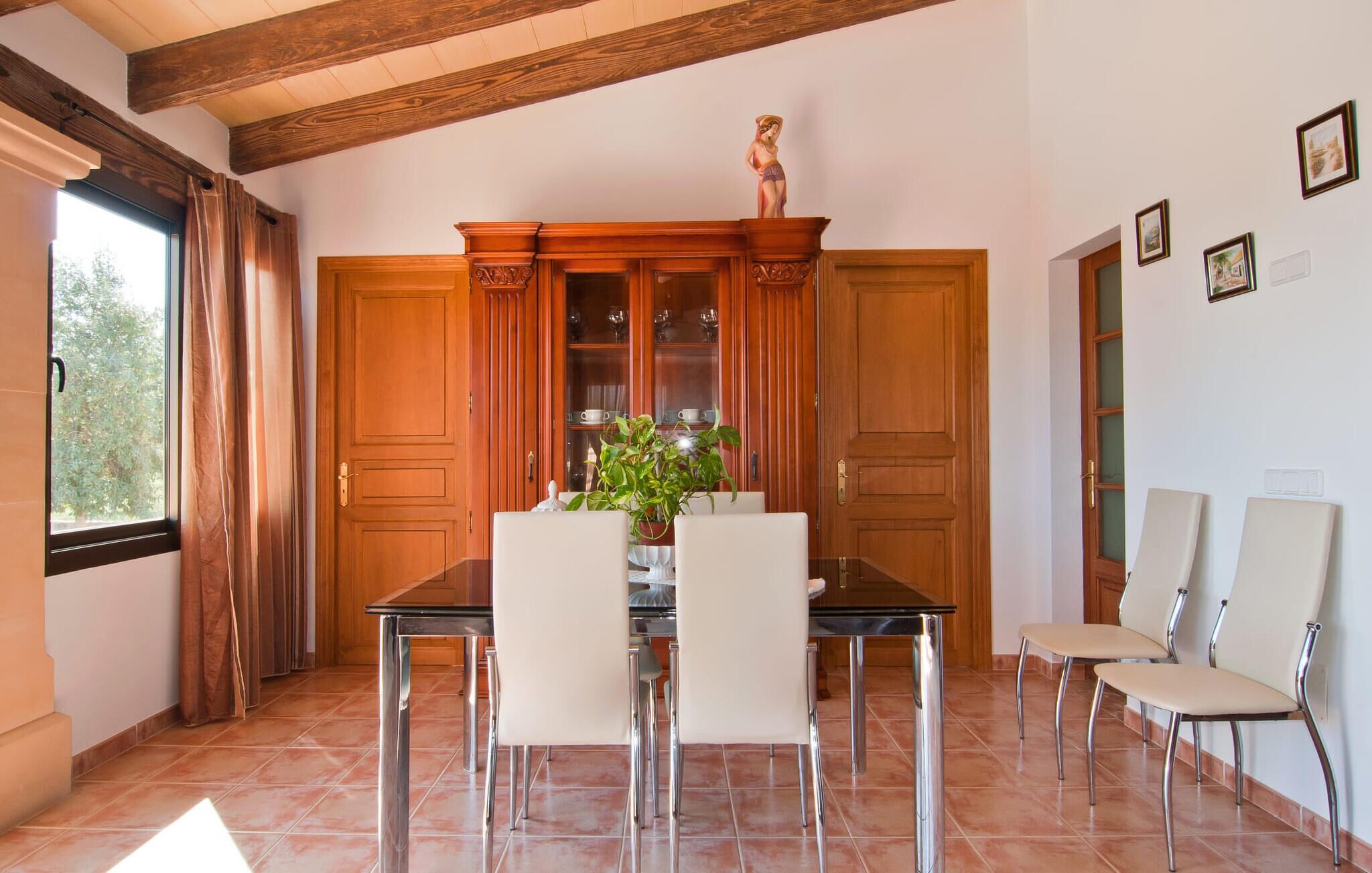 A dining area with a wooden cabinet, a statue, and a window with curtains.