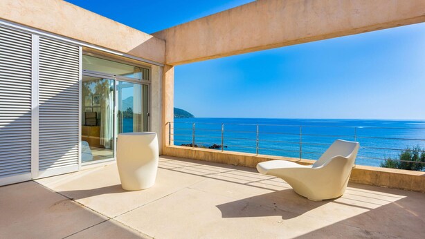Een balkon met twee witte stoelen, een glazen deur en uitzicht op zee.